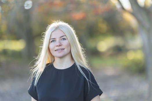 A young woman with braces, wearing a black shirt, poses for a picture in a park.