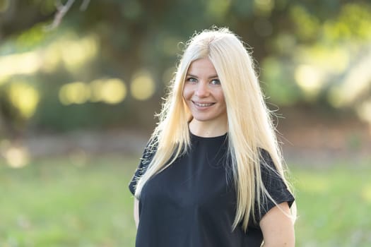 A young woman with long blonde hair standing confidently in a field, smiling brightly.