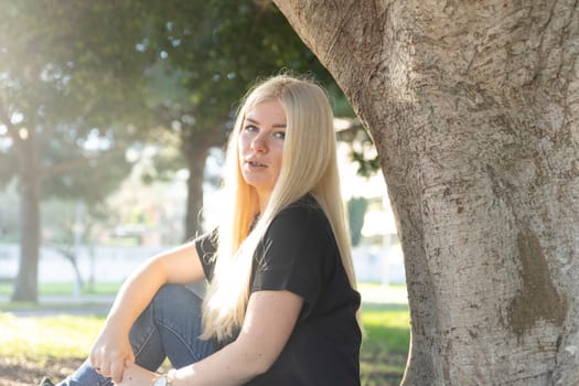 A young woman with braces sitting under a tree, smiling and enjoying the peaceful surroundings of a park on a sunny day.