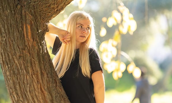 A young woman with braces is leaning against a tree in the park, smiling.