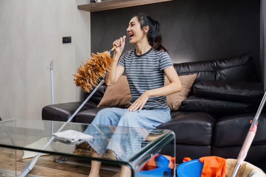 Asian woman happily use feather pick as microphone while cleaning house on the weekend.