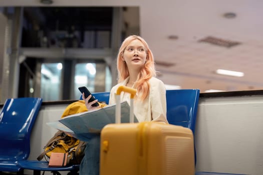 Happy young woman asian is sitting in airport near suitcase and reading map.