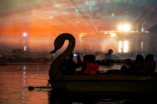 People in a swan shaped boat enjoying the light, sound and fountains show at Gadisar lake showing the famous tourist spot near Jodhpur and a place to relax in India