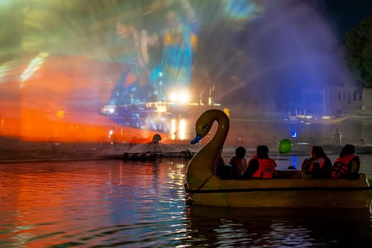 People in a swan shaped boat enjoying the light, sound and fountains show at Gadisar lake showing the famous tourist spot near Jodhpur and a place to relax in India