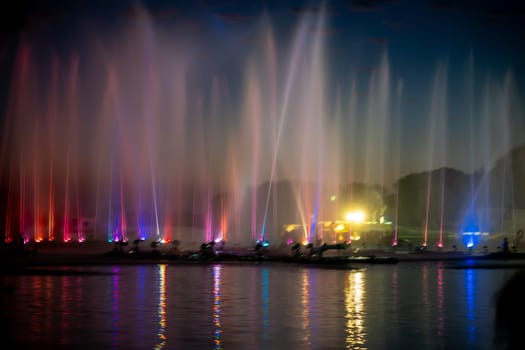 wide shot showing colorfully lit musical fountains public attraction on the famous tourist landmark Gadisar lake in Jaisalmer, Jodhpur Rajasthan with boats moving in front of it in India