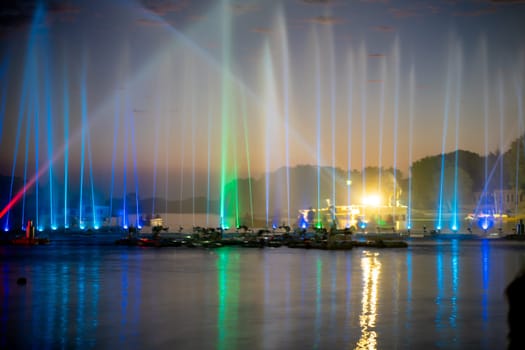 wide shot showing colorfully lit musical fountains public attraction on the famous tourist landmark Gadisar lake in Jaisalmer, Jodhpur Rajasthan with boats moving in front of it in India