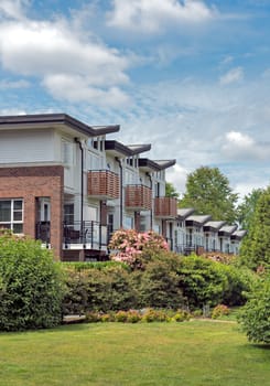 Row of residential townhouses on cloudy sky background with green lawn in front