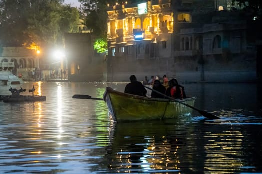 Family enjoying a night boat ride on the lit waters of Gadisar lake in Jaisalmer Jodhpur with the scenic palace and domes nearby a popular tourist destination India