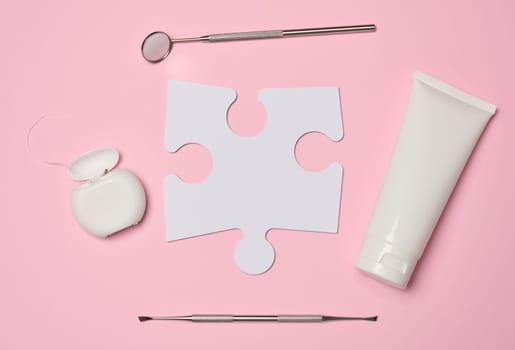 White tube with toothpaste, dental floss and paper puzzle on a pink background, top view