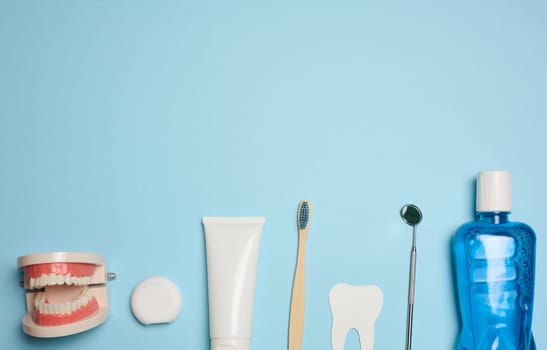 Mouthwash, toothpaste tube, dental floss and medical mirror on a blue background, oral hygiene. Top view