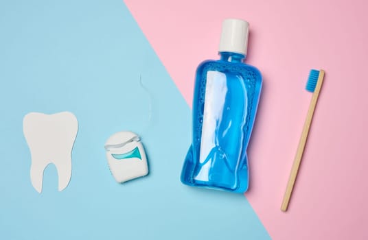 Plastic bottle with mouthwash, wooden toothbrush on blue background, top view