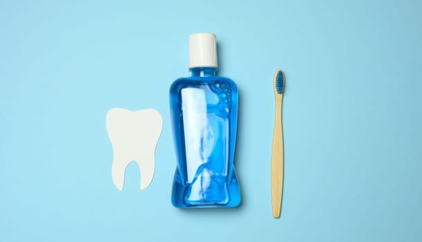 Plastic bottle with mouthwash, wooden toothbrush on blue background, top view