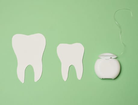 Dental floss and paper teeth on green background, oral hygiene, top view