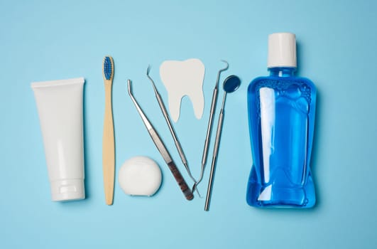 Mouthwash, toothpaste tube, dental floss and medical mirror on a blue background, oral hygiene. Top view