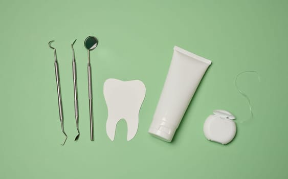 Tube with toothpaste, dental floss and medical mirror on a green background, oral hygiene. Top view