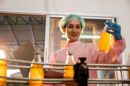 Managerial woman inspects bottles on machinery using laptop in factory. Quality control and liquid check ensure high industry standards. Technology-driven control is the key.