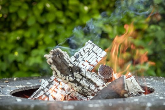 Close up shot of log pieces and fire wood, charcoal and ashes burning in flames in an old vintage brazier, in a blurred background.