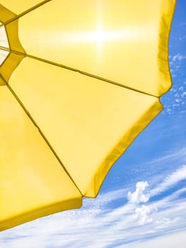 Yellow beach umbrella on blue sky with white clouds. Bottom view.