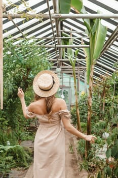 A beautiful young woman takes care of plants in a greenhouse. The view from the back. Concept of gardening and an eco-friendly lifestyle.