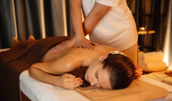 Caucasian woman customer enjoying relaxing anti-stress spa massage and pampering with beauty skin recreation leisure in warm candle lighting ambient salon spa at luxury resort or hotel. Quiescent