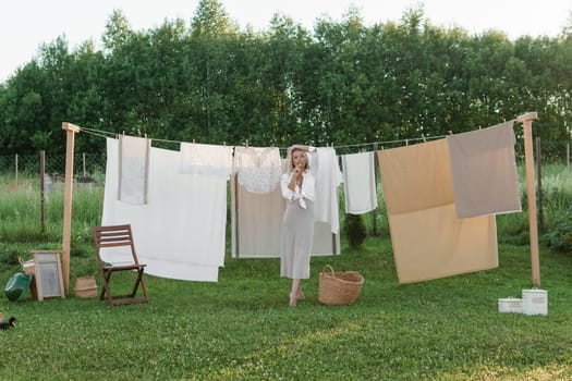 Laundry day. A woman hangs linen and towels on a tree in the courtyard of a village house. Summer cottage concept.