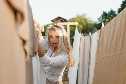 Laundry day. A woman hangs linen and towels on a tree in the courtyard of a village house. Summer cottage concept.