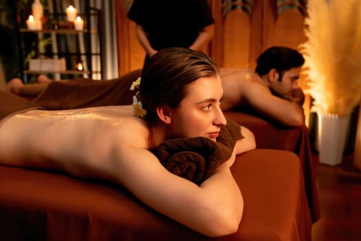 Caucasian couple customer enjoying relaxing anti-stress spa massage and pampering with beauty skin recreation leisure in warm candle lighting ambient salon spa at luxury resort or hotel. Quiescent