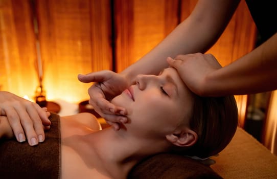 Caucasian woman enjoying relaxing anti-stress head massage and pampering facial beauty skin recreation leisure in warm candle lighting ambient salon spa in luxury resort or hotel. Quiescent