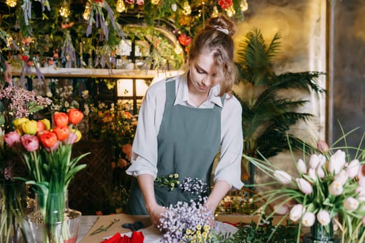 A woman in her florist shop collects bouquets of flowers. The concept of a small business. Bouquets of tulips for the holiday on March 8