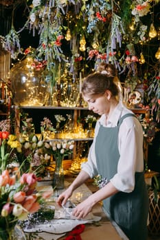 A woman in her florist shop collects bouquets of flowers. The concept of a small business. Bouquets of tulips for the holiday on March 8