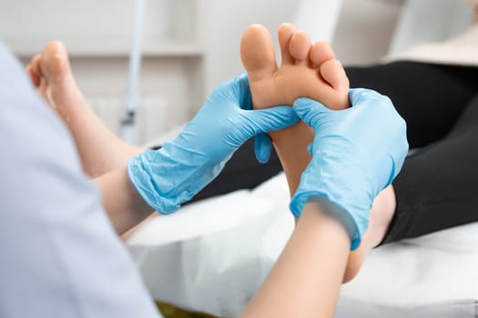 Skilled female masseur in rubber gloves giving foot massage to young woman at beauty salon.