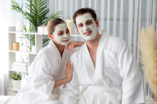 Blissful couple in bathrobe with facial cream mask enjoying serene ambiance of spa salon resort or hotel during holiday. Pampering face spa and skincare treatment with essence relaxation. Quiescent