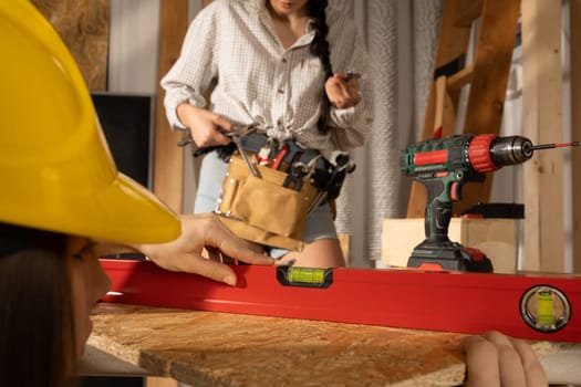 The blonde puts a red spirit level to the table top and the brunette checks if the indications are correct.