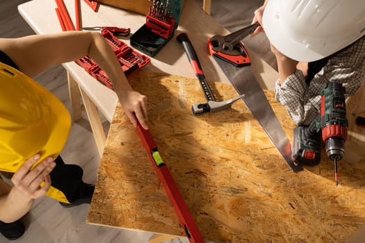 The blonde puts a red spirit level to the table top and the brunette checks if the indications are correct.