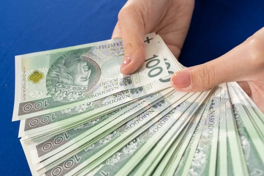 Green banknotes held in young female hands. Blue tablecloth on the table.