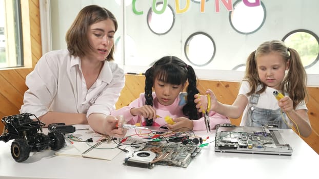 Skilled caucasian teacher teach and explain students about digital electrical tool. Expert girl learn electronic equipment and use to fix motherboard at table with chips and wires placed. Erudition.
