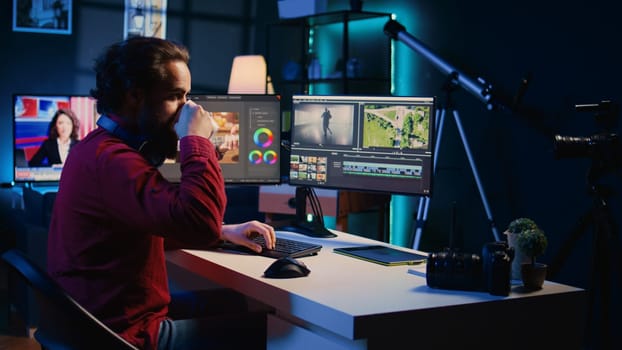 Video editor polishing raw footage, applying modern editing techniques in order to enhance clarity, sharpness and brightness. Videographer adjusting clips while enjoying cup of coffee in office