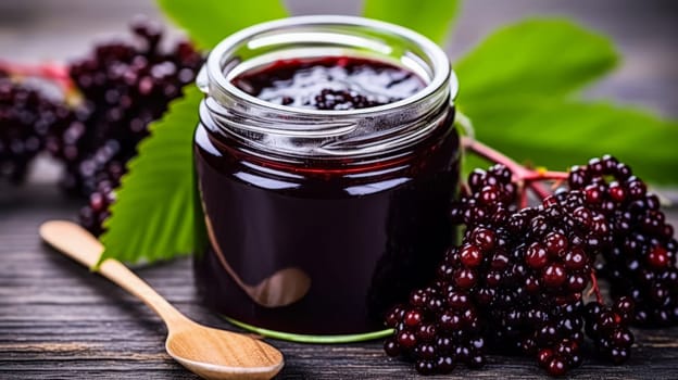 A jar of blackberry jam is sitting on a wooden table with a spoon next to it. The jar is filled with a deep purple liquid and surrounded by a bunch of blackberries. Concept of warmth and comfort