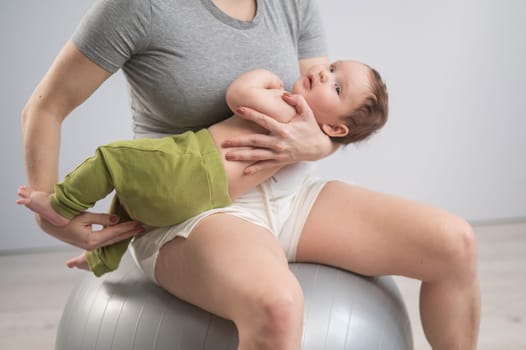 A faceless woman rocks her newborn son on a fitball