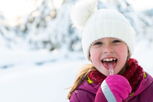 Cute little girl while eating icicle on beautiful winter day.