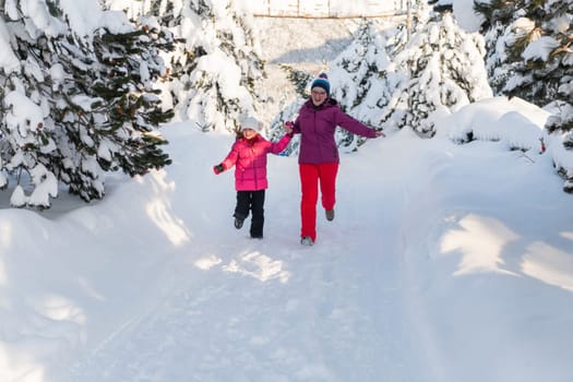 A mother and daughter as they dash along a serene snowy path, embracing the tranquil beauty of their winter mountain getaway.