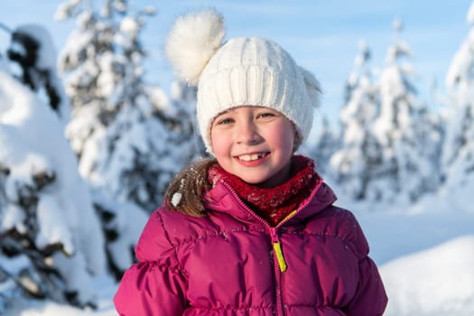 A radiant girl smiles against a backdrop of snow-capped mountains, the sun illuminating her joyful expression.