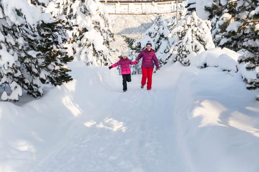 A mother and daughter as they dash along a serene snowy path, embracing the tranquil beauty of their winter mountain getaway.