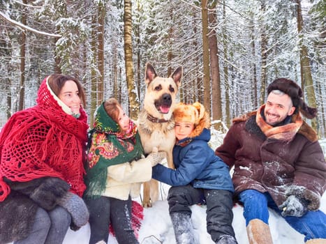 Joyful family ethnic dress with shawls and earflap hats and dog in winter forest in Russia carnival Maslenitsa. Tourists in Shrovetide in spring. Mother, father, son, daughter having fun in snow