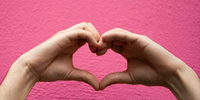 Hands forming a heart shape isolated on pink background.