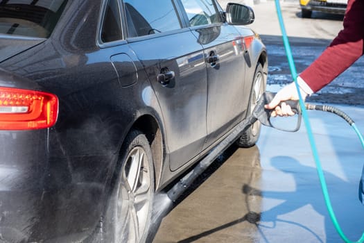 A man washes off the foam while washing the car. A vehicle is engulfed in soapy foam during a car wash, covering the tires, wheels, hood, and entire exterior of the car. Self-service car wash