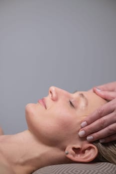Caucasian woman undergoing a head and face massage procedure. Vertical photo
