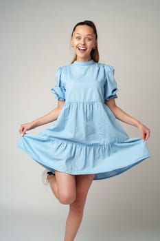 Young happy smiling woman in a light blue dress on a gray background close up