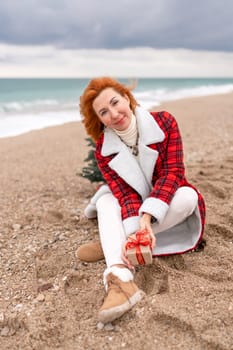 Lady in plaid shirt holding a gift in his hands enjoys beach with Christmas tree. Coastal area. Christmas, New Year holidays concep.