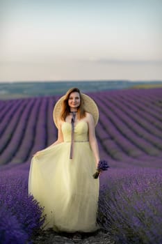 Woman poses in lavender field. Happy woman in yellow dress holds lavender bouquet. Aromatherapy concept, lavender oil, photo session in lavender.